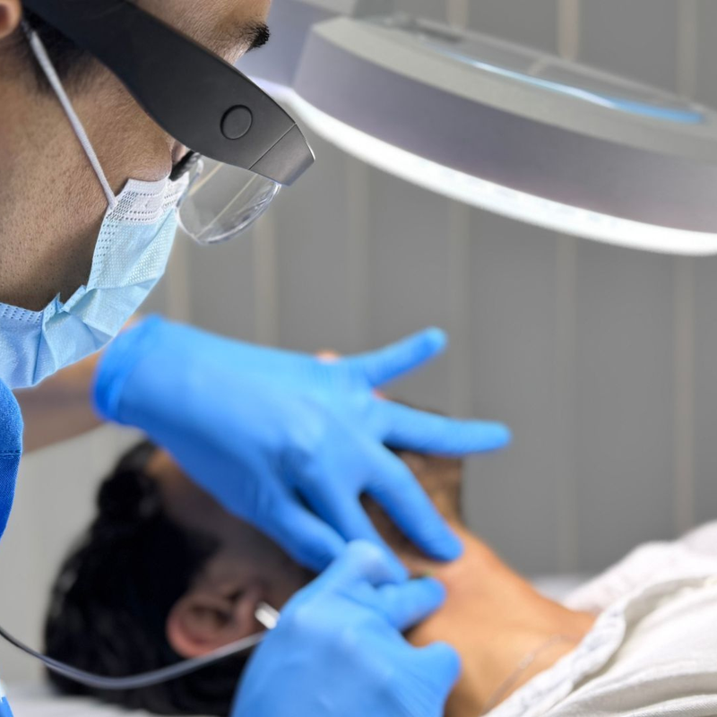 Person wearing blue gloves performing electrolysis on a male client